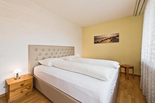a bedroom with a bed with white sheets and a table at Appartementhaus-Quadern in Valens