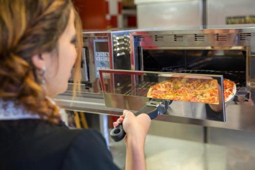 a woman is looking at a pizza in an oven at Hôtel Originals City, Armony Dijon - Chenôve in Chenôve