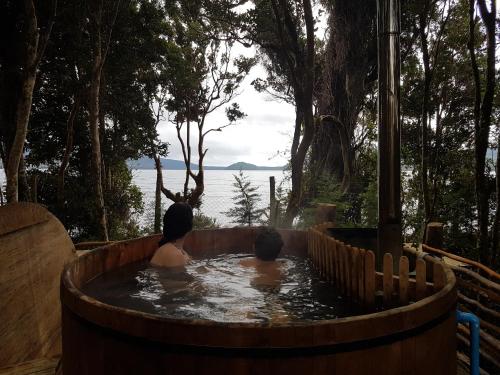 two people in a hot tub with a view of the water at Cabañas Torre Huillinco in Huillinco