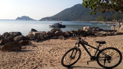 a bike parked on a beach with a boat in the water at Woodlawn Villas Resort in Koh Tao