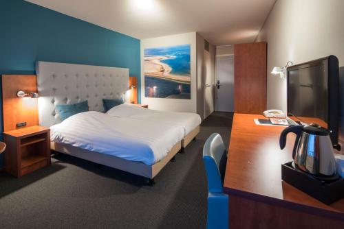 a bedroom with a large white bed and a desk at Hotel Lands End in Den Helder