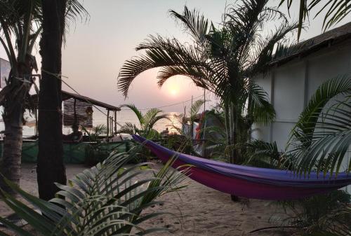 a hammock on a beach with a palm tree at Sea Front Beach Huts in Patnem