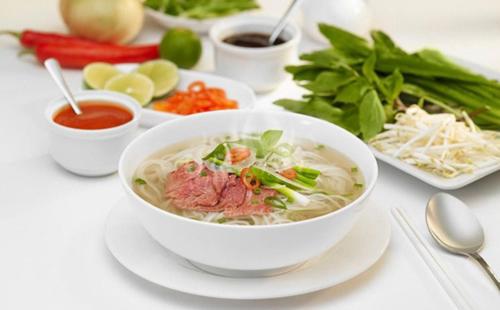 eine Schüssel Suppe auf einem Tisch mit anderen Lebensmitteln in der Unterkunft Nouveau Happy Inn - Bến Thành in Ho-Chi-Minh-Stadt