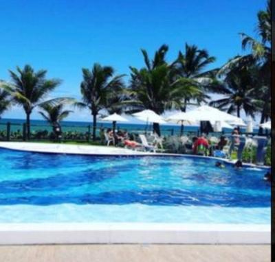 a large swimming pool with palm trees and the ocean at Genipabu Summer House Guarajuba in Guarajuba