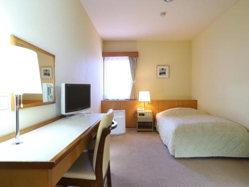 a bedroom with a bed and a desk with a television at Asahikan in Shiojiri