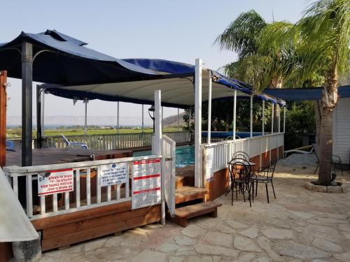a covered deck with a table and chairs and a palm tree at The Lake House in Migdal