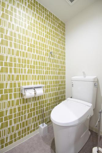 a bathroom with a toilet and a yellow tiled wall at Guest House Re-worth Joshin1 3F in Nagoya