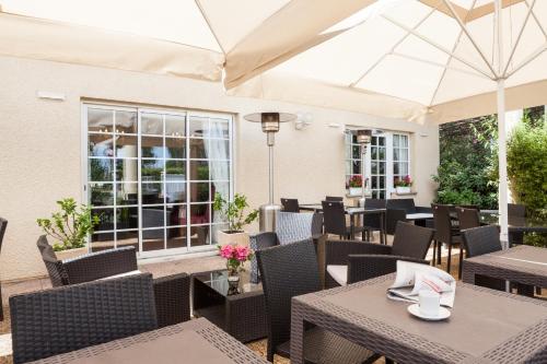 d'une terrasse avec des tables, des chaises et un parasol. dans l'établissement The Originals City Hôtel Bordeaux Porte du Bassin, à Gradignan