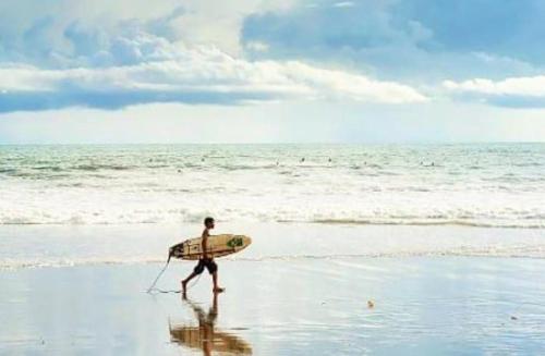 a man walking on the beach with a surfboard at The Lookout Beach Hotel in San Lorenzo