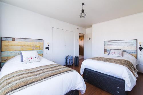 2 camas en un dormitorio con paredes blancas y suelo de madera en Mapa Hostel, en Osorno