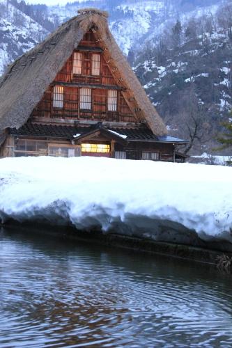 a house with a thatched roof next to the water at Gokayama Onsen Akaokan in Nanto