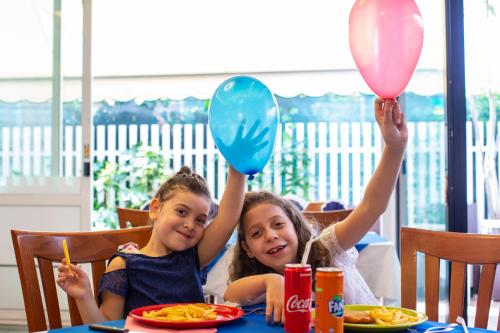 two girls sitting at a table holding up balloons at Hotel Holland in Rimini