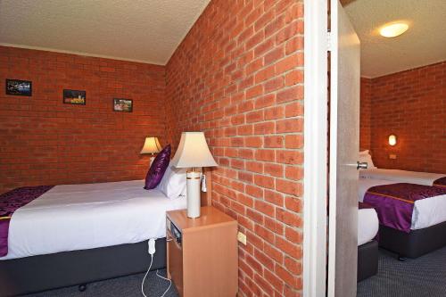 a room with two beds and a brick wall at Main Lead Ballarat Motel in Ballarat