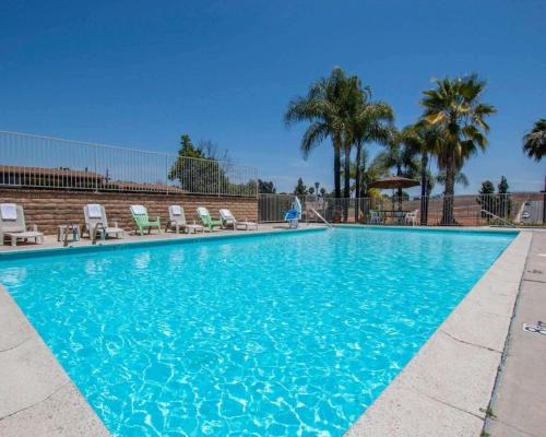 a large blue swimming pool with chairs and palm trees at Rodeway Inn Fallbrook Downtown in Fallbrook