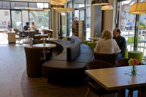 Menschen sitzen in einem Restaurant mit Tischen und Stühlen in der Unterkunft Aparthotel Landau an der Isar in Landau an der Isar