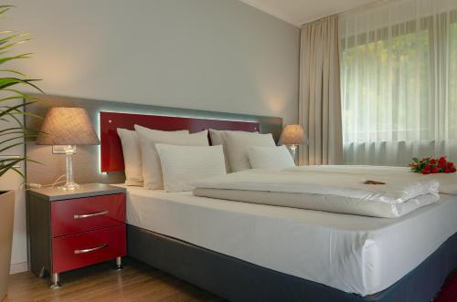 Waldhotel Sindelfingen am Eichholz في شيندلفينجن: غرفة نوم مع سرير كبير مع منضدة حمراء