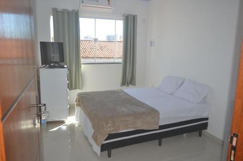 Habitación blanca con cama y ventana en Suítes Centro, en Arraial do Cabo