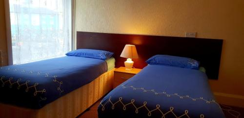 ブラックプールにあるHotel Avano - Pleasure Beachのベッドルーム1室(青いシーツとランプ付きのベッド2台付)
