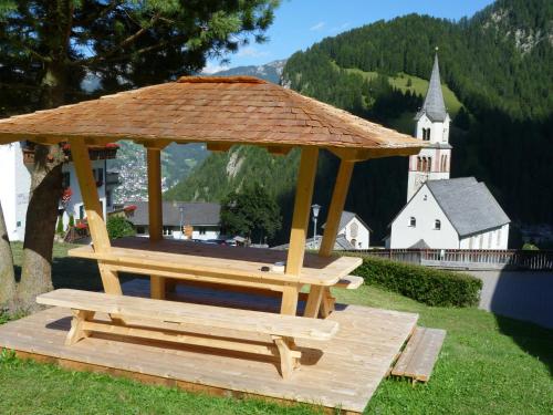 a wooden gazebo with a bench and a church at Garni Kostner in Ortisei