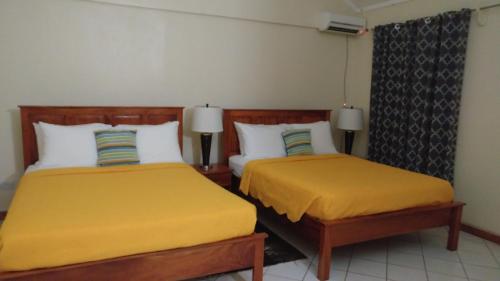 two beds in a hotel room with yellow sheets at Classique International in Dominica in Marigot