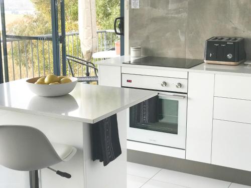 a white kitchen with a bowl of fruit on a counter at Tamar River Apartments in Rosevears