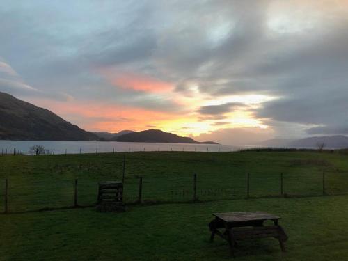 a picnic table in a field with the sunset in the background at Highland Croft B&B in Onich
