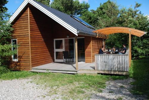 a cabin with a deck with two people sitting at a table at Hytteby – Hanstholm Camping – Thy Feriepark in Hanstholm