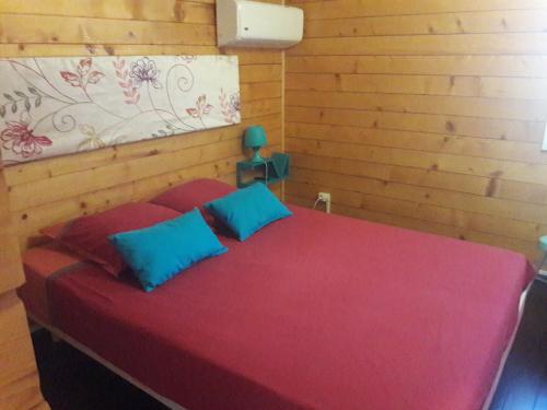 a red bed with two blue pillows in a room at chambre d' hôte village sauvage in Langevin