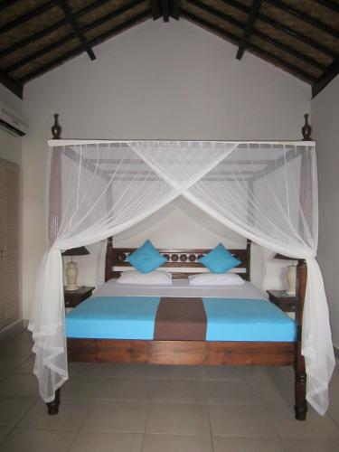 a bedroom with a canopy bed with blue pillows at Kembali Beach Bungalows in Amed