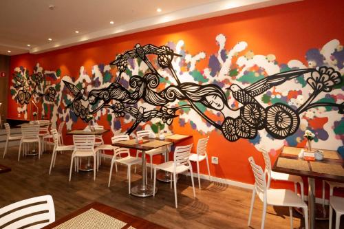 uma sala de jantar com mesas e cadeiras em frente a um mural em Royal Design Savassi Hotel em Belo Horizonte