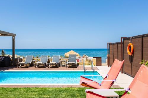 a swimming pool with chairs and a table and the ocean at Espera, Luxury Beach Front Residence, By ThinkVilla in Rethymno