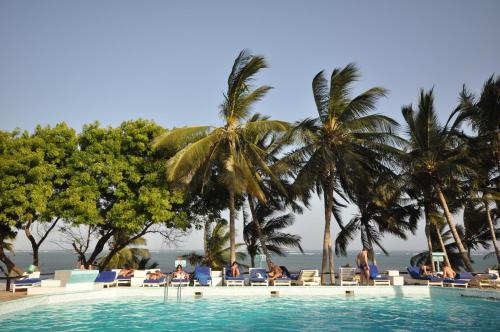 a swimming pool with palm trees and people sitting in chairs at Baobab Sea Lodge in Kilifi