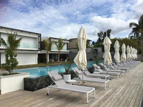 una fila de tumbonas con sombrillas junto a una piscina en OBiches Luxury Beachfront Apartment Trou-aux-Biches, en Trou aux Biches