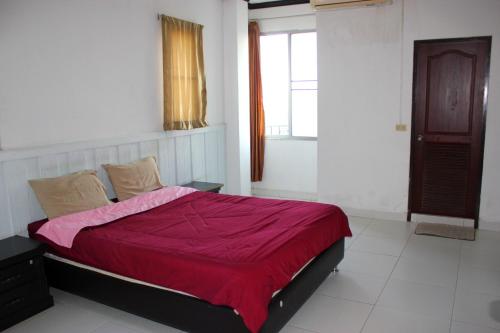 a bedroom with a bed with a red comforter and a window at Matini Amata in Ban Hua Phai