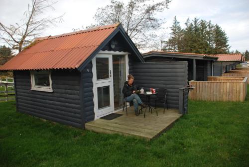 a woman sitting at a table in a tiny house at Hytteby – Hanstholm Camping – Thy Feriepark in Hanstholm