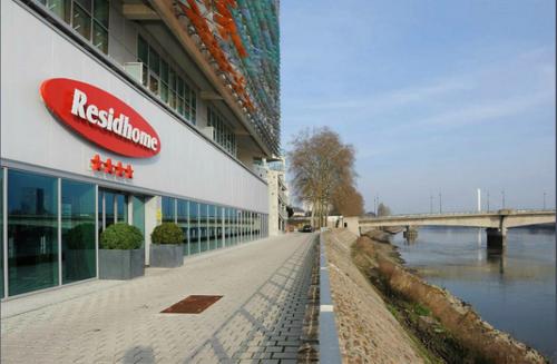 a building with a red sign on it next to a river at Residhome Nantes Berges De La Loire in Nantes