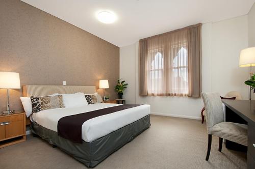 a bedroom with a large bed with a desk and a chair at Adabco Boutique Hotel Adelaide in Adelaide