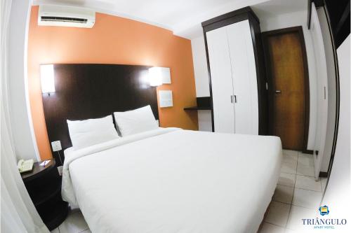 a bedroom with a large white bed and an orange wall at Triângulo Apart Hotel in Vitória