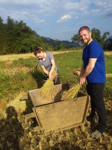 a man and a woman standing in a field with a wheelbarrow of hay at ChienDe Homestay in Sa Pa
