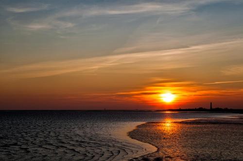 a sunset on the beach with the sun setting at Gud Jard Lodge Nr 25 - Design-Ferienhaus mit exklusiver Ausstattung in Pellworm