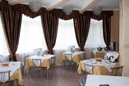 un restaurante con mesas y sillas blancas y ventanas en Pansionat Mechta, en Kislovodsk