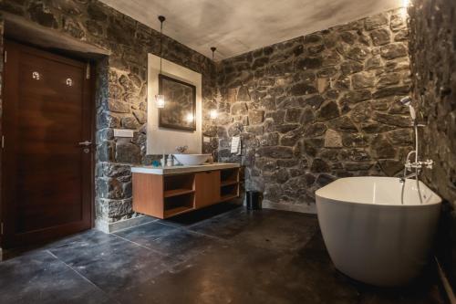 a bathroom with a tub and a stone wall at Elakai in Munnar