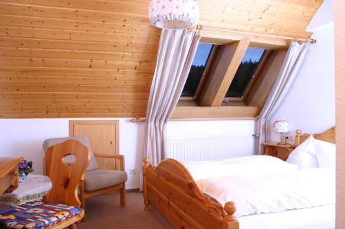 a bedroom with a bed and a chair and two windows at Pension Mühlencafé in Breitnau