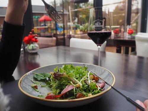 a bowl of salad on a table with a glass of wine at Boutique Hotel, Restaurant & Wellness Westerburcht in Westerbork