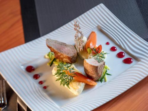 a white plate with meat and vegetables on a table at Garrigae Manoir de Beauvoir Poitiers Sud - Hotel & Spa in Mignaloux-Beauvoir