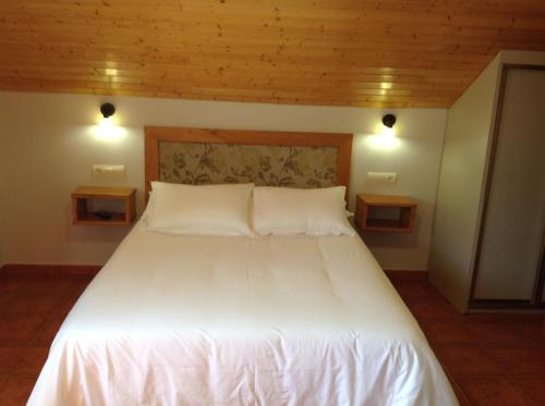 1 cama blanca grande en una habitación con 2 luces en Alojamiento en entorno rural Los Trobos, en Villar de Otero
