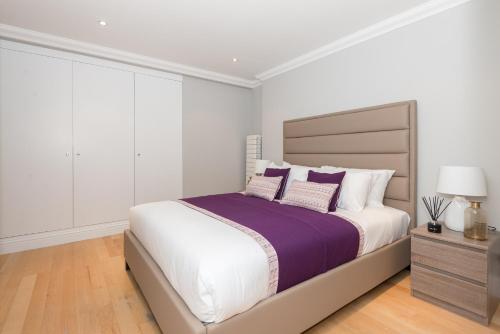 ein weißes Schlafzimmer mit einem großen Bett mit lila und weißen Kissen in der Unterkunft One bedroom Hyde Park Apartment in London