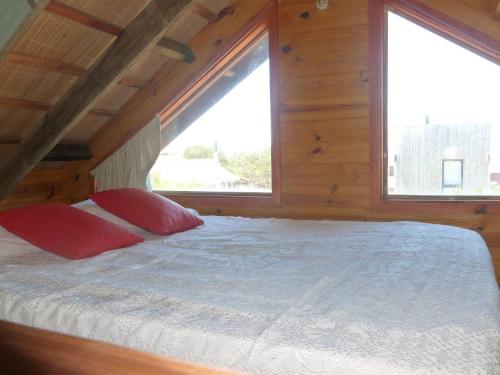 1 cama con 2 almohadas rojas en una habitación con 2 ventanas en Excelente Cabaña Cumbre del Diablo 2, en Punta del Diablo