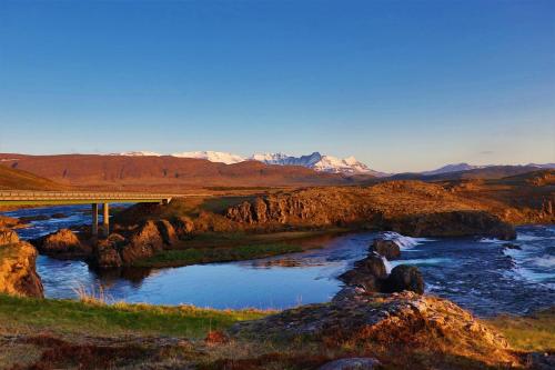 a bridge over a river with mountains in the background at Fossatún Sunset Cottage in Fossatún