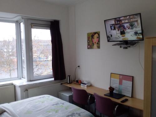 een slaapkamer met een bureau, een bed en een televisie bij Hotel Baan in Rotterdam
